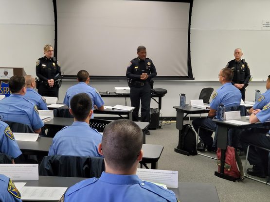Image of new recruit class in a classroom with Chief Scott